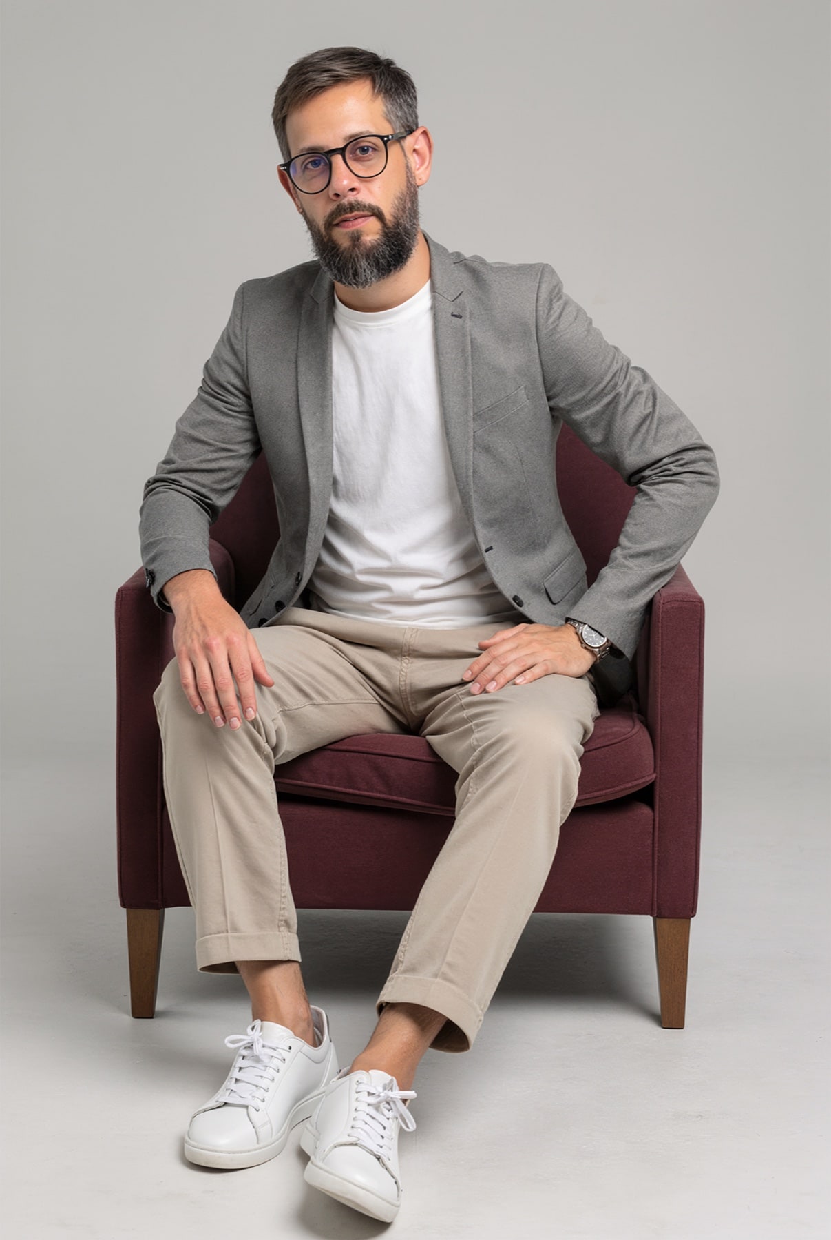Guilherme Eugênio Ronconi sentado em uma poltrona, usando blazer cinza e óculos