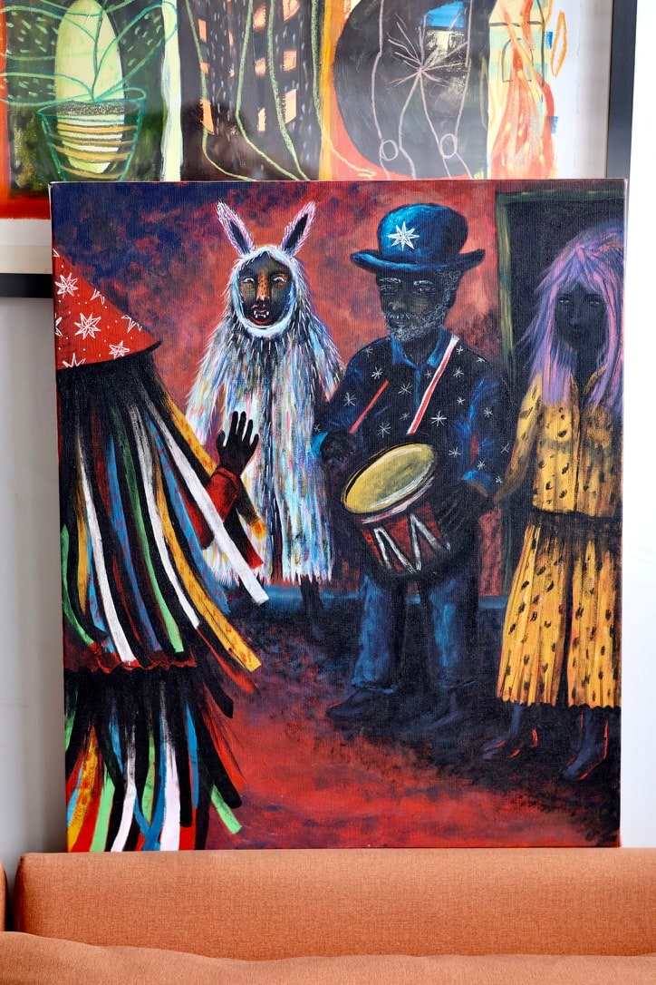 Figuras de um cortejo com máscaras, roupas coloridas e tambor